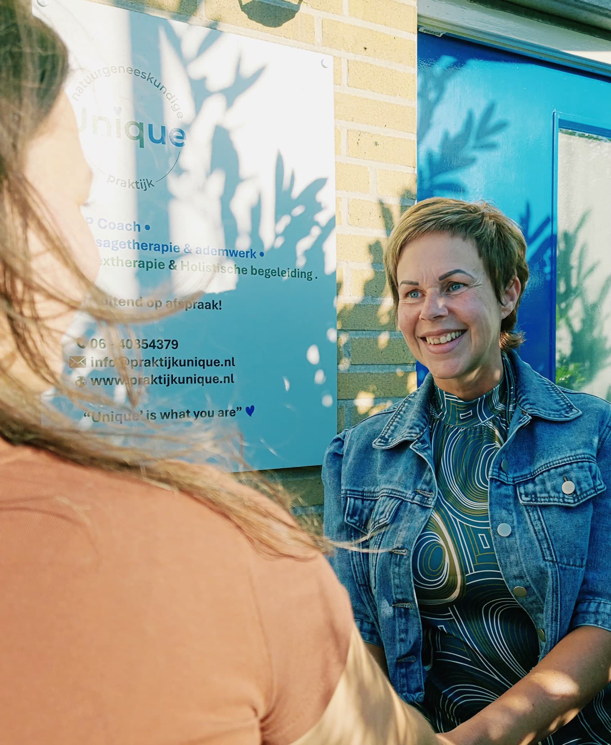 Sandra Peereboom lachend bij het bord van Praktijk Unique